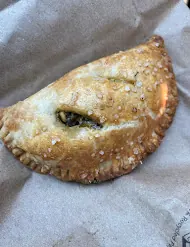 A hand-folded savory empanada with a golden, sesame-flecked crust